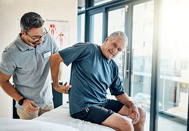 Physiotherapy, chiropractor and senior man with back pain for rehabilitation, consulting and exercise. Healthcare, physical therapy and person with patient for medical service, wellness and support.